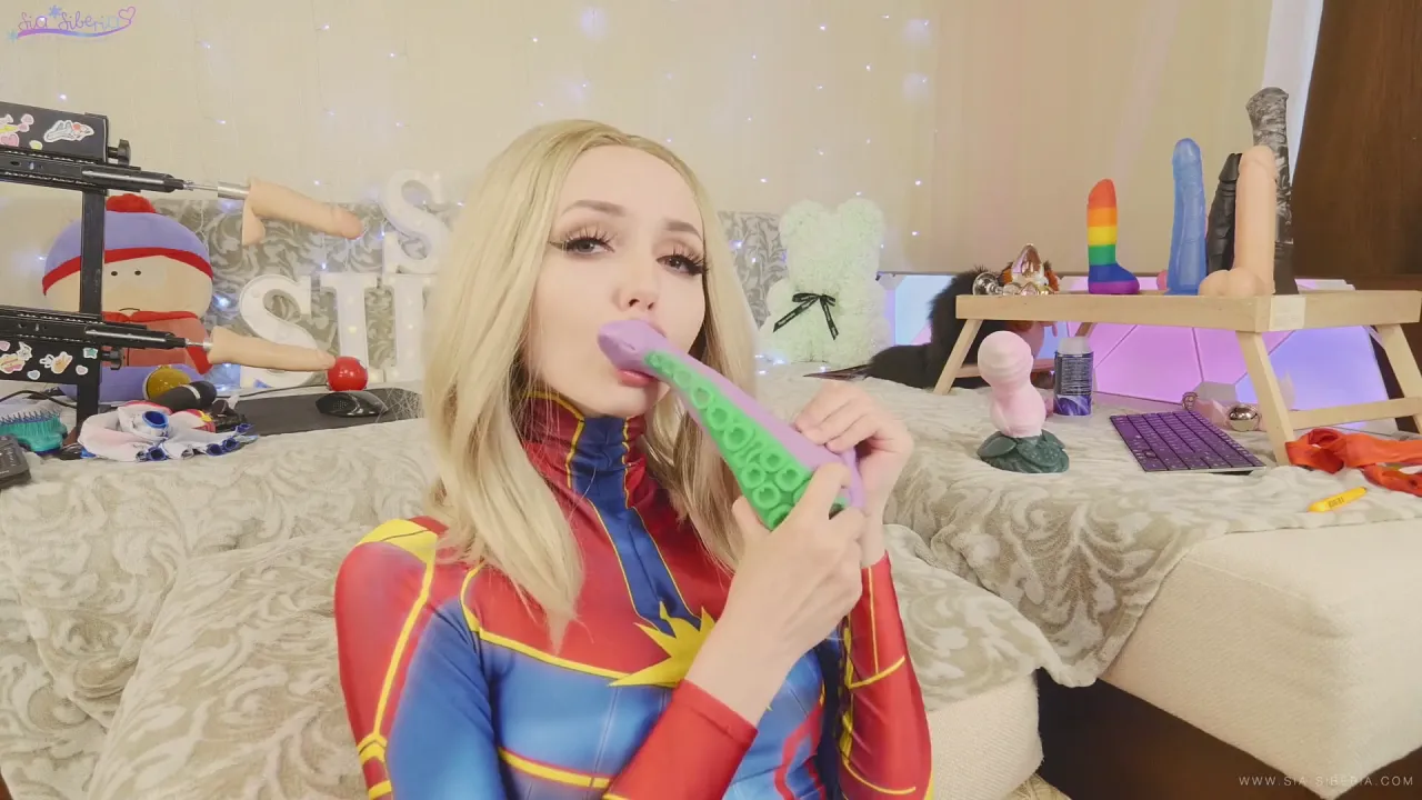 Captain Marvel cosplaying blonde sucks dildo and fingers her wet pussy